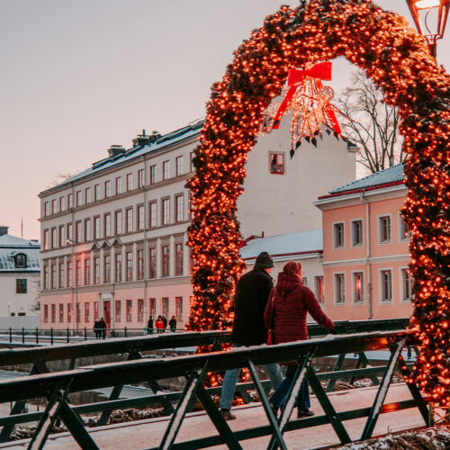 Ett par går över en bro dekorerad med med juliga, lysande girlanger