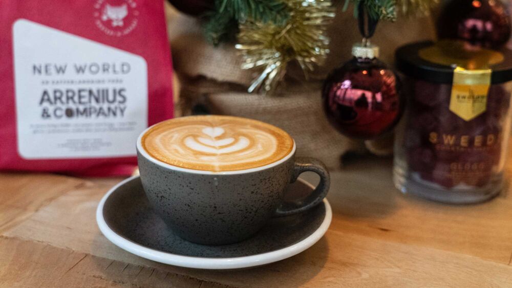 En kopp kaffe, en minijulgran och en röd påse med kaffebönor på ett träbord