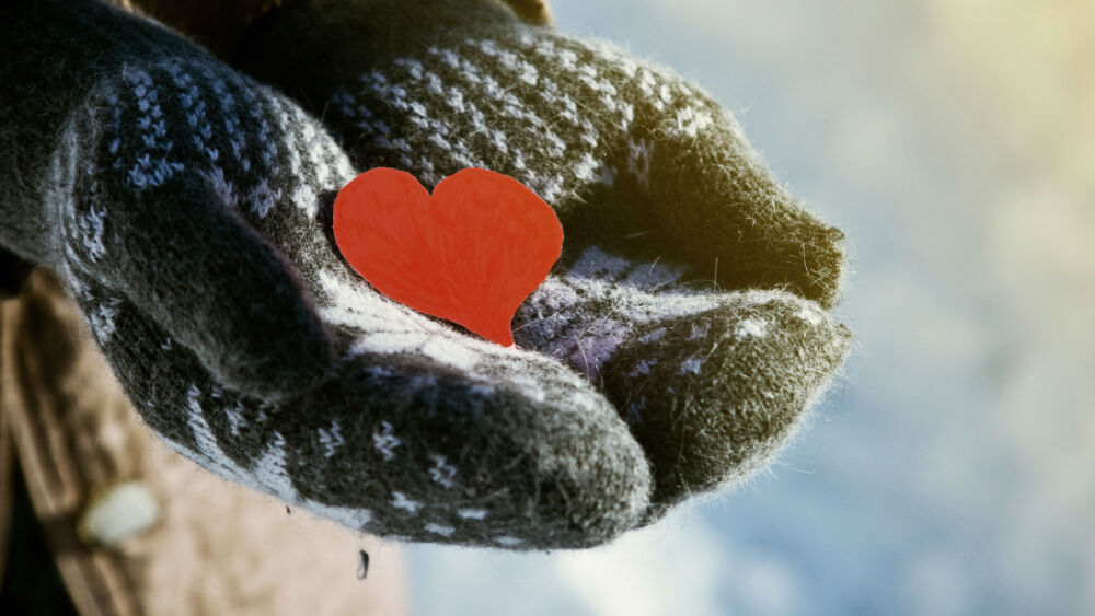 Närbild på vantbeklädda händer som håller i ett rött pappershjärta
