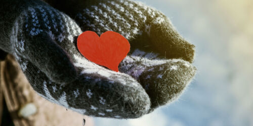 Närbild på vantbeklädda händer som håller i ett rött pappershjärta