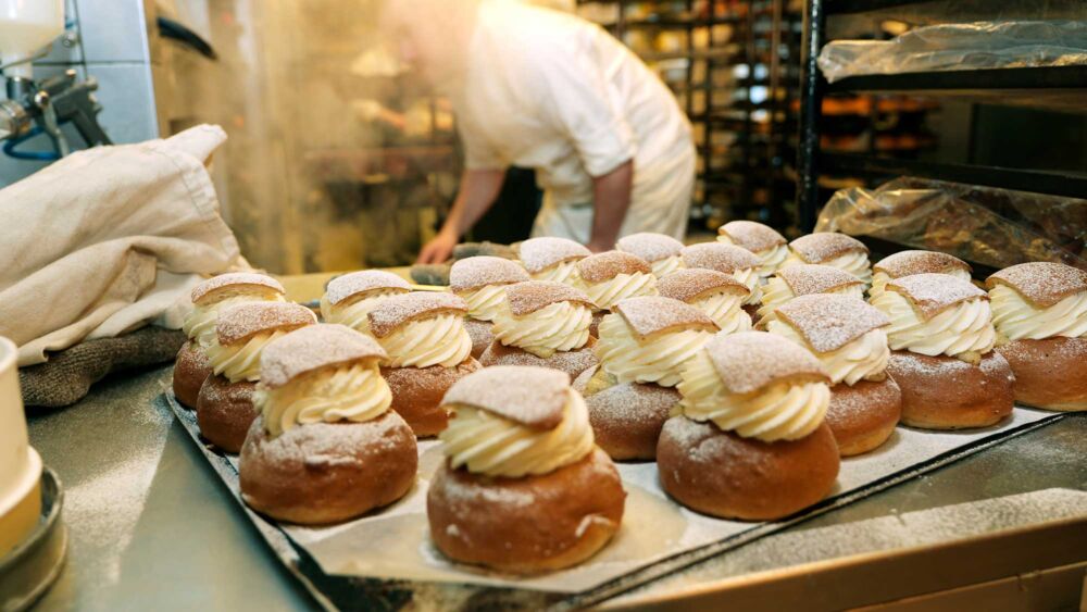 Närbild på flera semlor på en plåt i bagerimiljö
