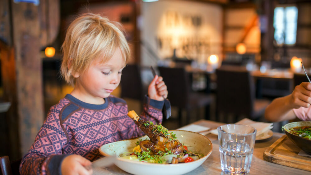 Preschool child, cute boy, eating lamb meat in a restaurant, cozy atmosphere, local small restaurant in Tromso
