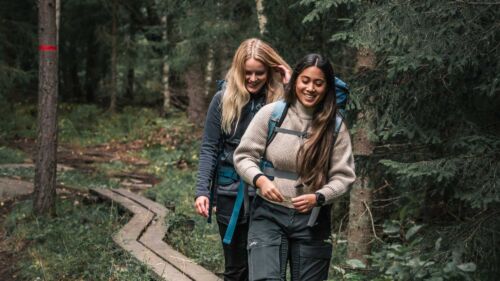 Två kvinnor i vandringskläder går i skogen i Uppsala