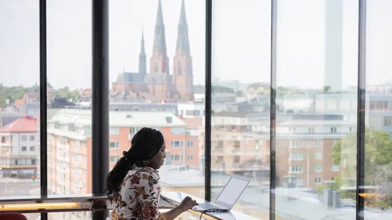 Kvinna jobbar på laptop på UKK i Uppsala med utsikt över domkyrkan