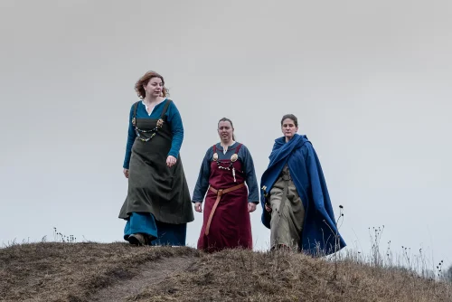 Tre personer i vikingakläder gåendes på Gamla Uppsala högar
