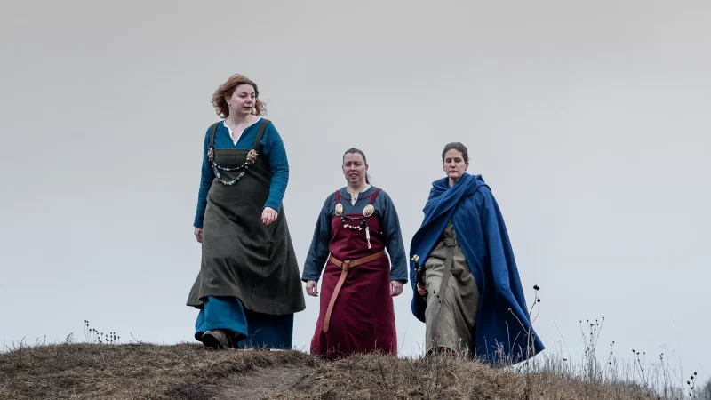 Tre personer i vikingakläder gåendes på Gamla Uppsala högar