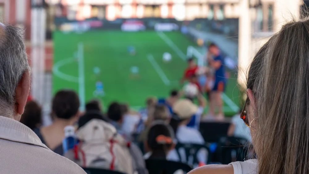 Personer kollar på fotboll på en stor skärm utomhus
