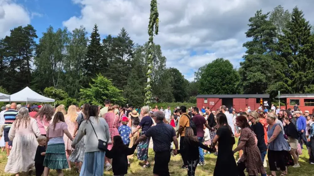 En grupp människor dansar runt en midsommarstång